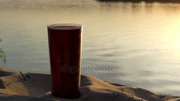 Una taza de café de plástico en una orilla del lago en una bonita puesta de sol en verano — Vídeo de stock