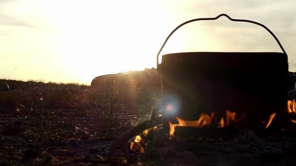 Un grand chaudron se tient dans un feu de camp. Il fait bouillir l'eau chaude au coucher du soleil au ralenti — Video
