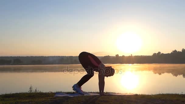 Mujer delgada se para en sus manos y dedos de los pies y salta al atardecer — Vídeos de Stock