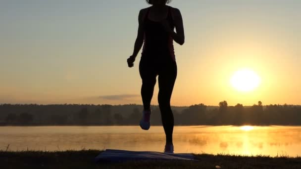 Жінка біжить в одному місці на березі озера на заході сонця в шлю-мо — стокове відео