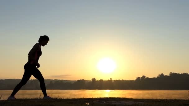 Mujer delgada corre hacia atrás y salta hacia adelante al atardecer — Vídeos de Stock