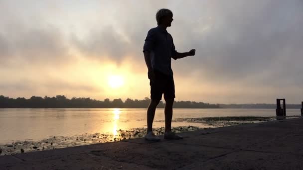 Atleta da la vuelta felizmente en una orilla del río con caña al atardecer en cámara lenta — Vídeos de Stock