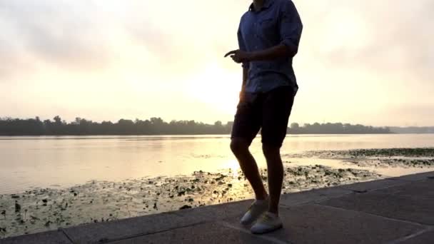 Feliz homem caminha, dança, vira-se em uma margem do rio ao pôr do sol em Slo-Mo — Vídeo de Stock