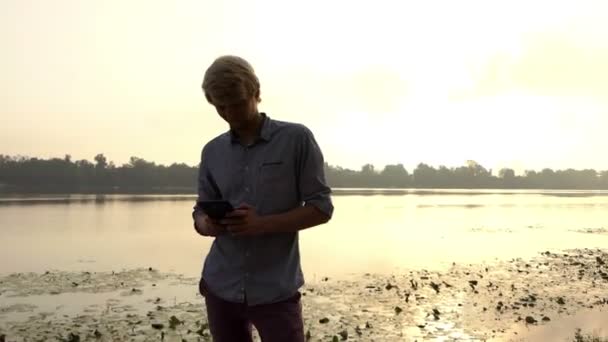Young Man Looks at His Smartphone And Dreams Outdoors at the Dnipro — Stock Video