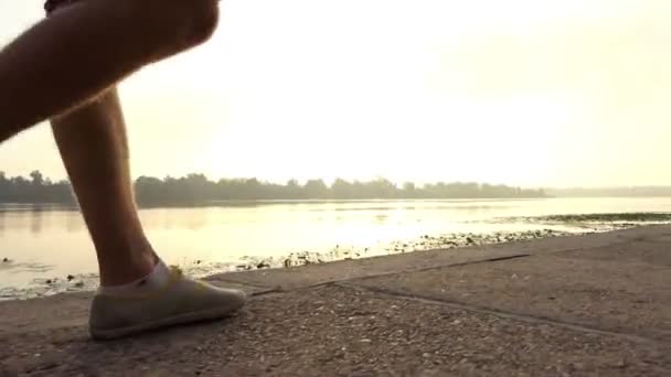 Jóvenes piernas de hombre caminan a lo largo de la orilla del río en verano — Vídeos de Stock
