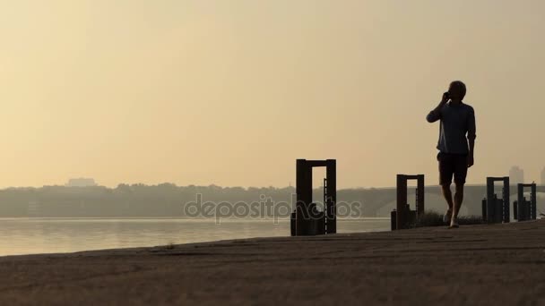 Giovane uomo cammina mentre parla sul suo cellulare al Dnipro al tramonto — Video Stock