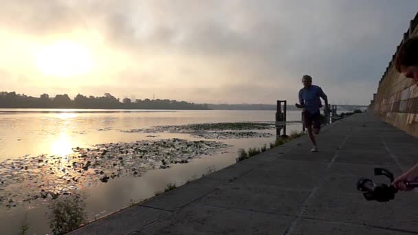 Jovem corre rápido ao longo da margem do rio Dnipro concreto ao pôr do sol em Slo-Mo — Vídeo de Stock