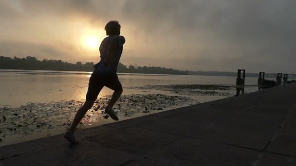 Deportista corre en la orilla del río cubierto con losas de hormigón al atardecer en Slo-Mo — Vídeos de Stock