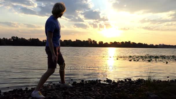 Schöner Sonnenuntergang und ein Mann wirft flache Steine ins Flusswasser in slo-mo — Stockvideo