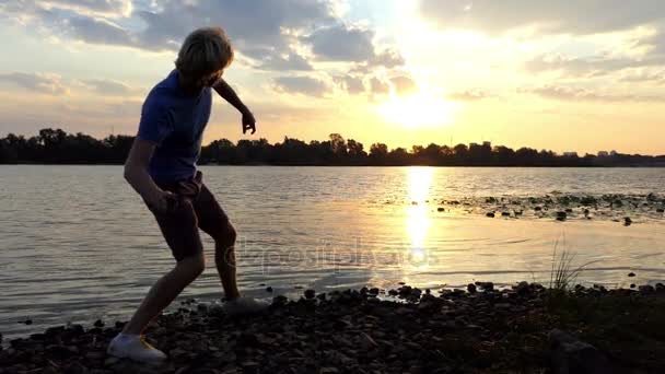 Junger Mann wirft bei einem herrlichen Sonnenuntergang in Slo-mo Aster ins Flusswasser — Stockvideo