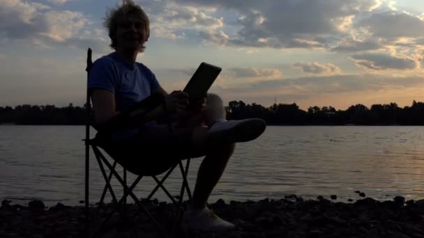 Ljusa Blogger mannen sitter på en hopfällbar stol och ser på sin surfplatta — Stockvideo