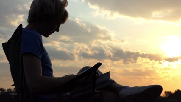 Smart Blogger senta-se em uma cadeira dobrável e olha para seu tablet ao pôr do sol — Vídeo de Stock