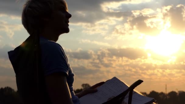 Talentovaný muž sedí, přečte a zapíše jeho poznámky na břehu při západu slunce — Stock video