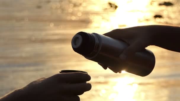 男性の手がスローモーションで日没で川岸にカップにフラスコから水を注ぐ — ストック動画