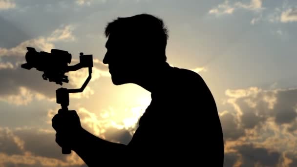 Junger Mann schießt mit einer Steadicam. es dreht sich um und überrascht ihn bei Sonnenuntergang — Stockvideo