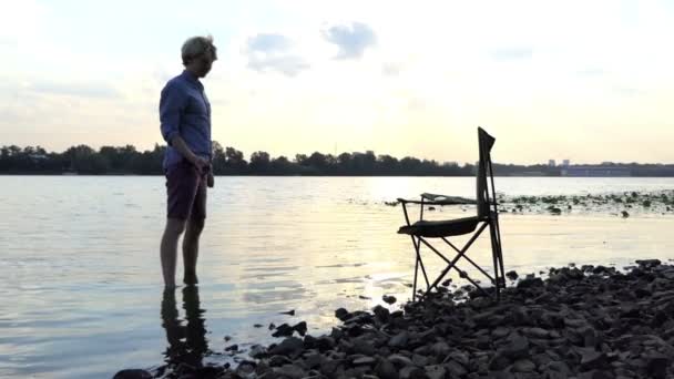 Junger Mann steht barfuß im Wasser an einem Flussufer und hütet einen Stein im Slo-mo — Stockvideo