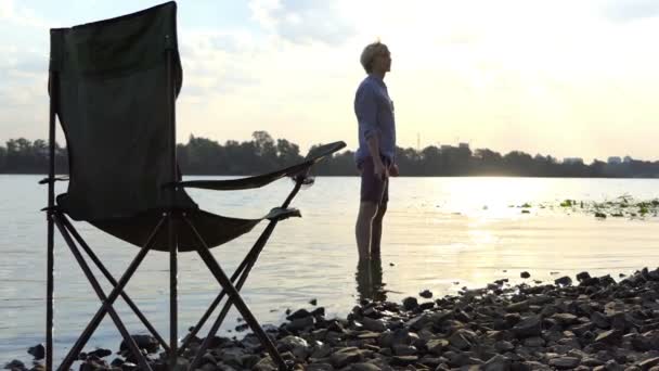 Štíhlý muž stojí bosky ve vodě na břehu a drží kámen v Slo-Mo — Stock video