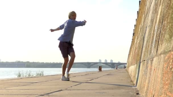 Спортивный человек танцует диско на берегу реки с каменной стеной летом в Slo-Mo — стоковое видео