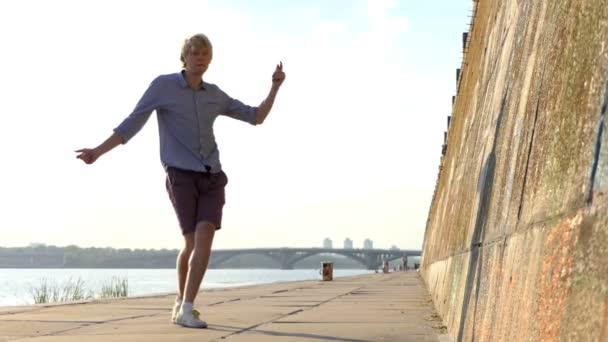 Homem esportivo dança disco em uma margem do rio com uma parede de pedra alta em Slo-Mo — Vídeo de Stock