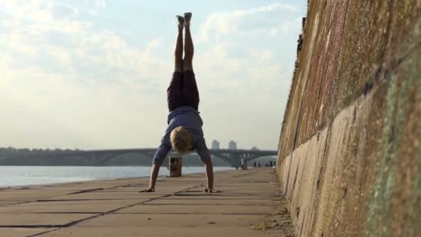 Jovem dança Disco e fica em suas mãos em uma margem do rio — Vídeo de Stock