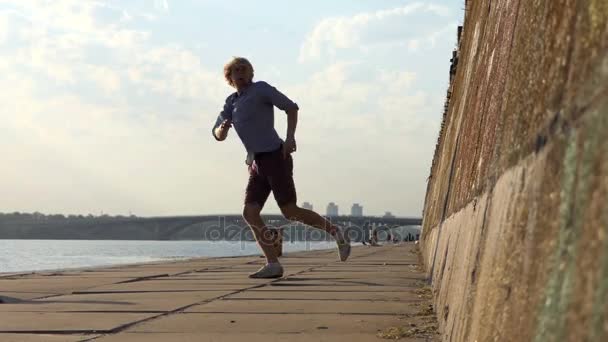 Young Man Dances Rock-N-Roll on a Riverbank With a High Wall in Summer — Stock Video