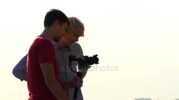 Двоє молодих людей стояти і подивитися на Stedicam, з нового відео на відкритому повітрі — стокове відео