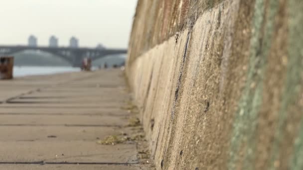 Un banquillo y una pared de piedra en el Dnipro con un puente en el fondo — Vídeo de stock