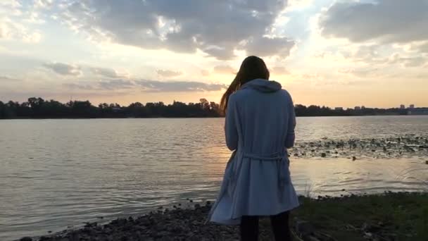 Joven mujer embarazada se para en una espléndida orilla del río al atardecer — Vídeos de Stock