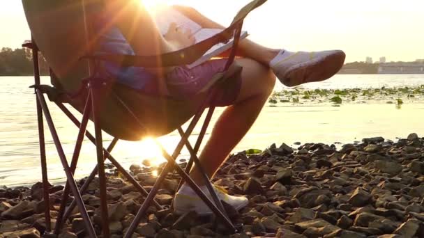 L'homme est assis, rêve, écrit quelque chose dans un bloc-notes, sur une rive à Slo-Mo — Video