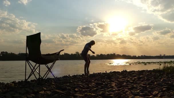 Умный человек стоит босиком в воде на берегу реки и бросает камень в Сло-Мо — стоковое видео