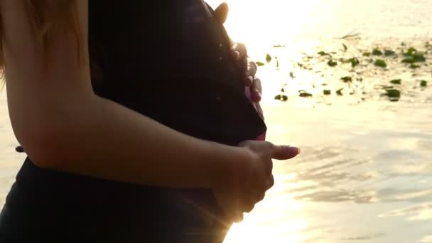 Mains féminines Tapez le ventre enceinte sur une rive au coucher du soleil à Slo-Mo — Video