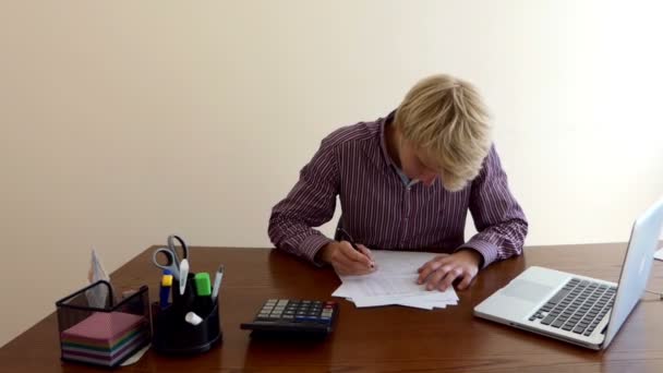 Man skriver ett dokument ser ut på en miniräknare, sitter vid ett bord på ett kontor — Stockvideo