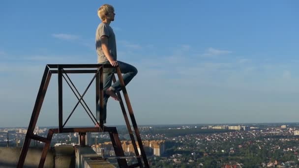 Молодой человек стоит на лестнице на высоком доме в замедленной съемке — стоковое видео