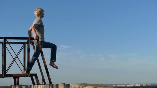 Young man stands on a metallic ladder on a high house - suicide — Stock Video