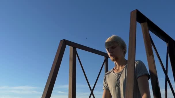 Yoga praktijk - een jongeman zit op een metalen ladder van een huis — Stockvideo