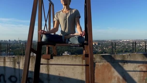 Blond man trains yoga on a high industrial building in summer — Stock Video