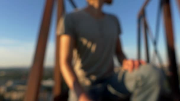 Jongeman zit op een metalen platform op een hoog gebouw bij zonsondergang. — Stockvideo