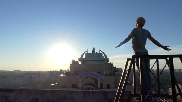 O jovem senta-se em um corrimão de uma escada em um edifício no pôr do sol — Vídeo de Stock