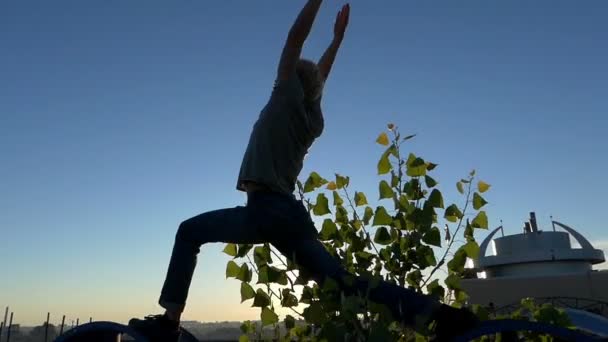 Homem loiro faz um guerreiro asana em duas rodas dentadas ao pôr do sol em slo-mo — Vídeo de Stock