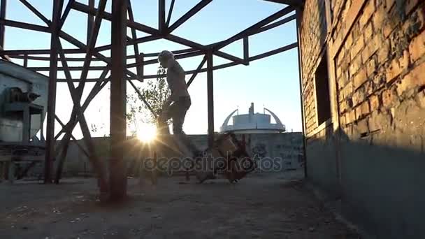 Muž s blond vlasy skáče na staveništi při západu slunce