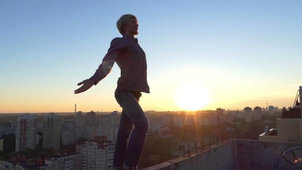 Dappere man staat op een rand van een hoge bouwplaats bij zonsondergang in slo-mo — Stockvideo