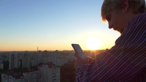 Biondo uomo guarda il suo cellulare su un cantiere alto al tramonto . — Video Stock