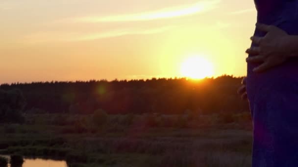 Gravid kvinna klappar magen på sjön bank vid solnedgången i slo-mo — Stockvideo
