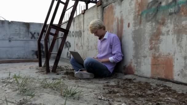 Blonda mannen sitter på en byggarbetsplats och arbetar på sin laptop — Stockvideo