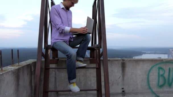 Δημιουργική άνθρωπος κάθεται σε μια μεταλλική πλατφόρμα υψηλής και χρησιμοποιεί τον υπολογιστή του σε slo-mo — Αρχείο Βίντεο