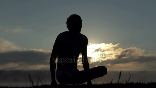 Sprawny człowiek siedzi na brzegu jeziora i praktyki jogi o zachodzie słońca w zwolnionym tempie — Wideo stockowe