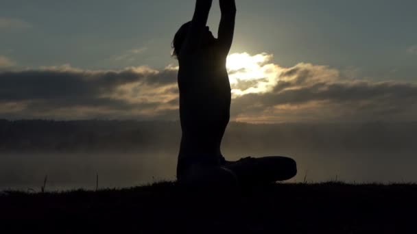 Духовный человек сидит на берегу озера и практикует йогу на закате в замедленной съемке — стоковое видео
