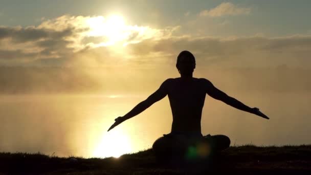 Leuchtender Yogi sitzt im Lotus auf einem Seeufer und betet bei Sonnenuntergang in Zeitlupe. — Stockvideo