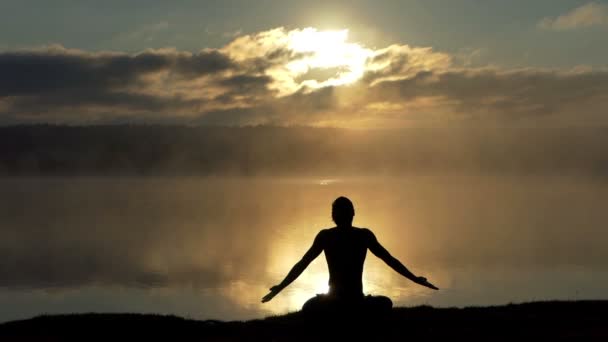 Andliga yogi sitter i lotus på sjön bank och ber vid solnedgången i slow motion. — Stockvideo