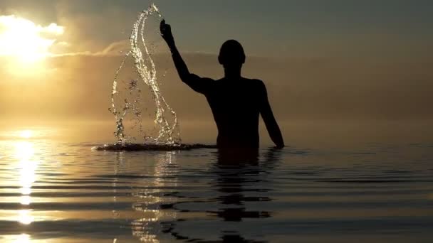 Hombre arty levanta arroyos de agua en un lago al atardecer en slo-mo — Vídeos de Stock